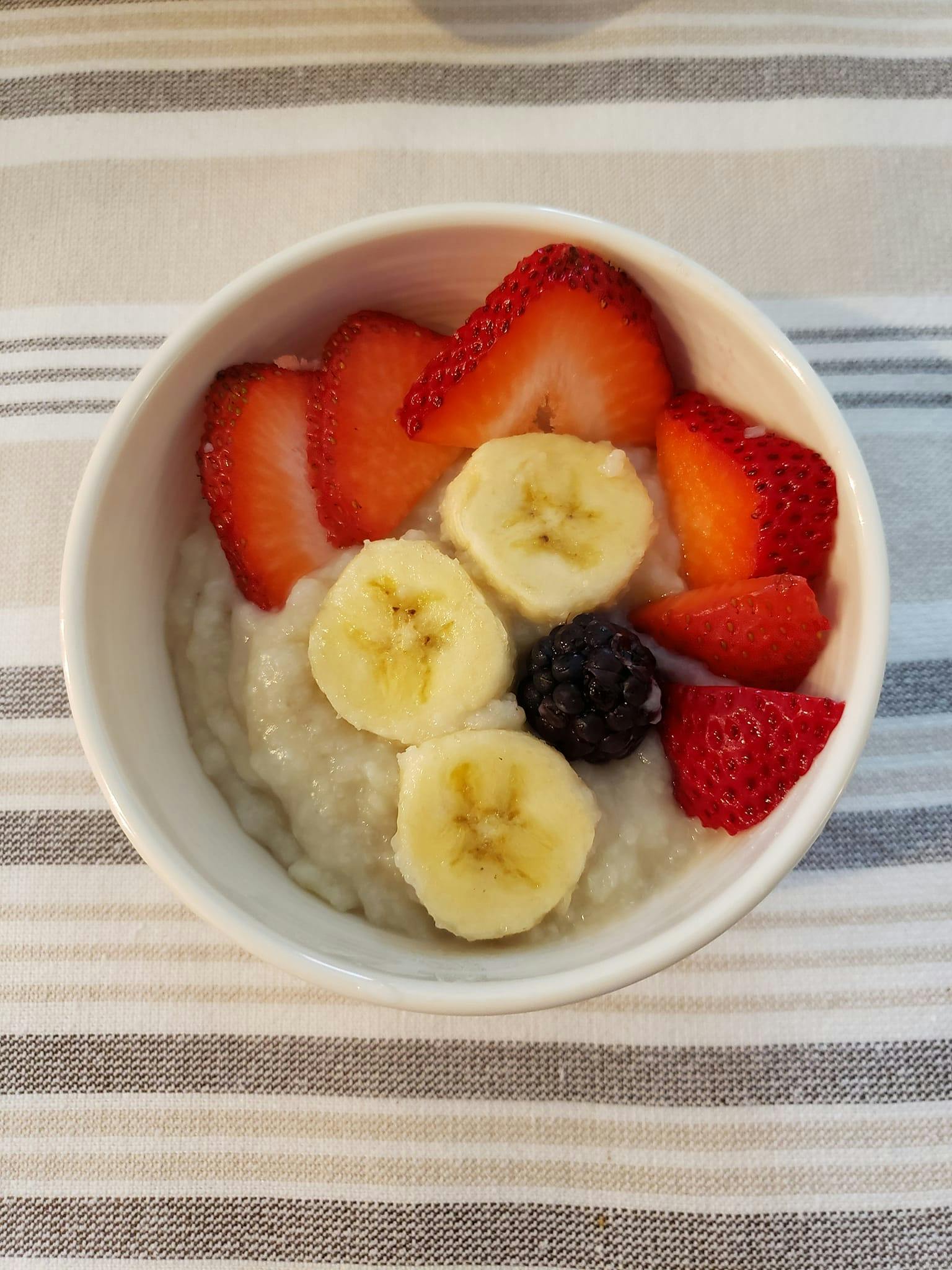 Bowl of oatmeal topped with sliced strawberries, bananas, and a blackberry