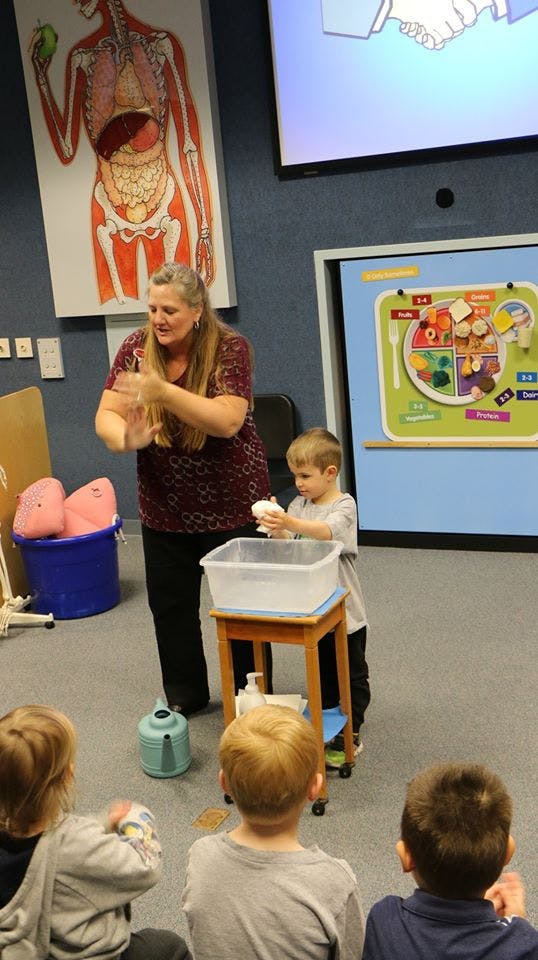 Adult and child washing hands over a basin, other children watching