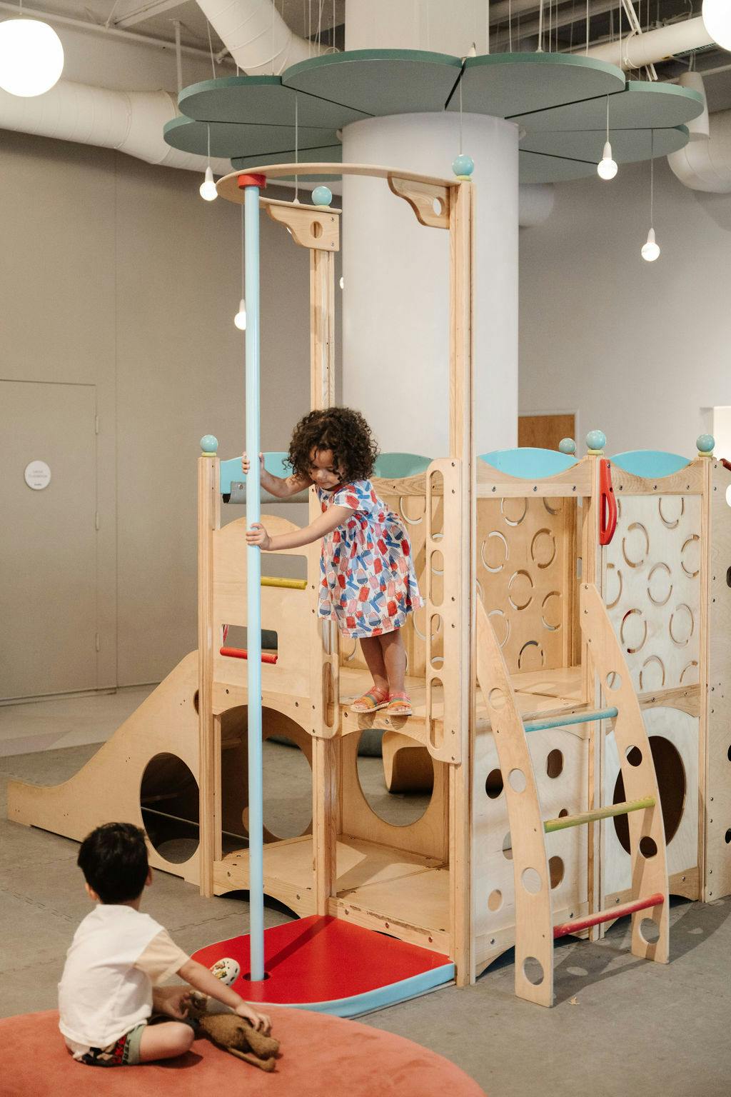 Child on a wooden play structure, another child sitting nearby