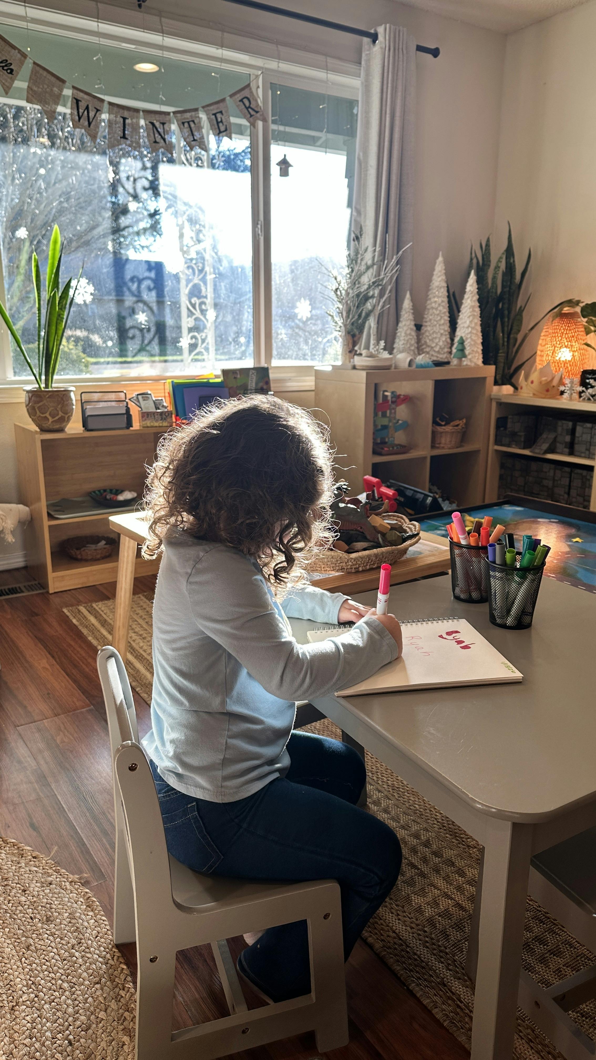 Child sitting at a table writing in a notebook with a pink marker