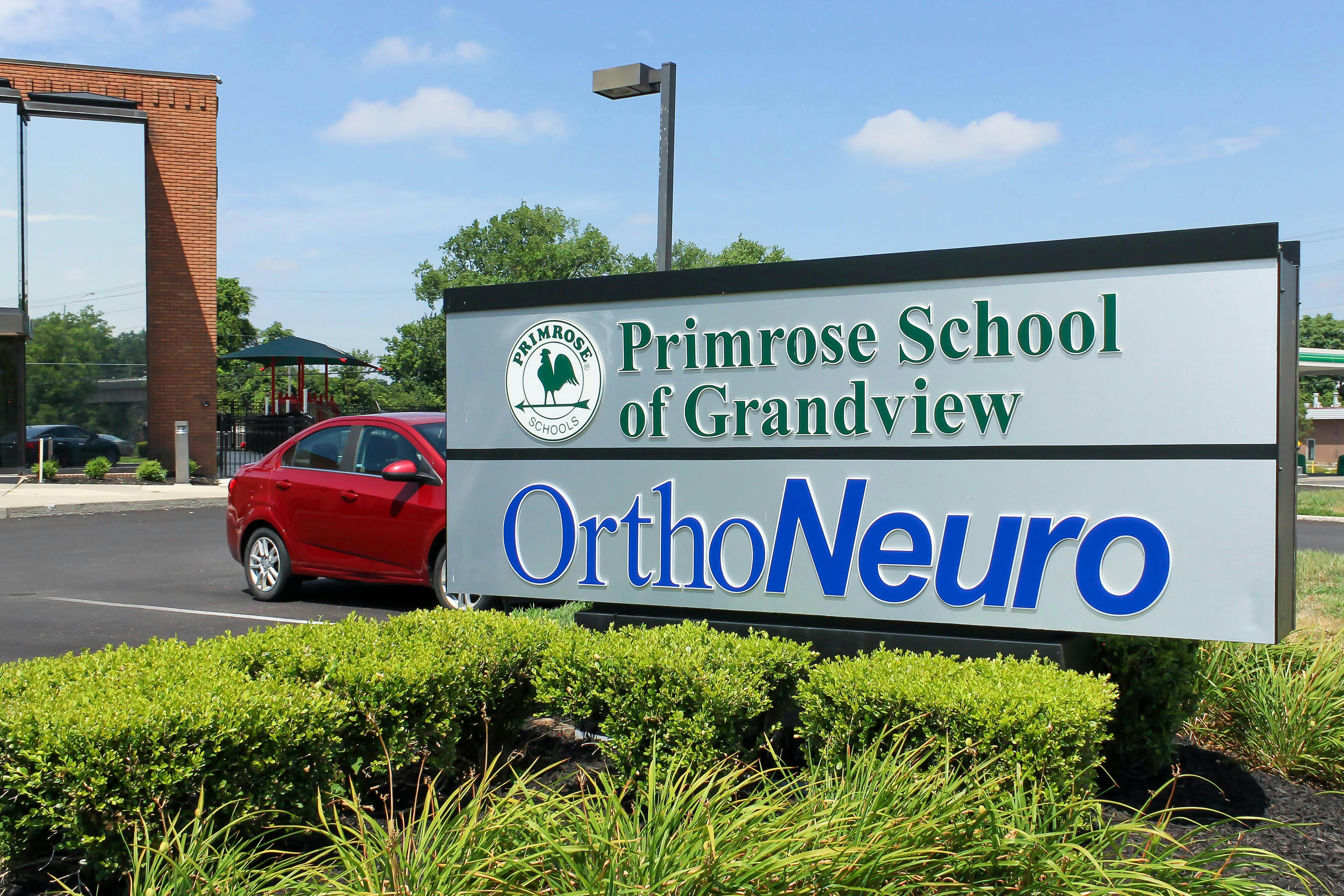 Sign for Primrose School of Grandview and OrthoNeuro with a red car nearby