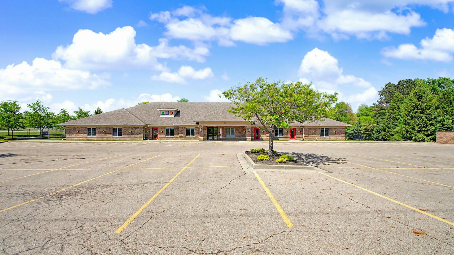 An empty parking lot in front of a long brick building with a brown roof