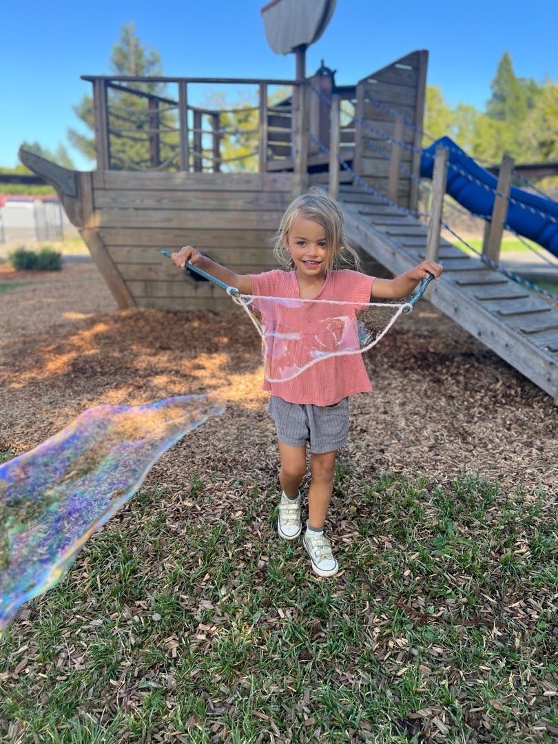 Child blowing a large bubble with a bubble wand on a playground