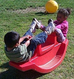 Two children playing on a red seesaw rocker