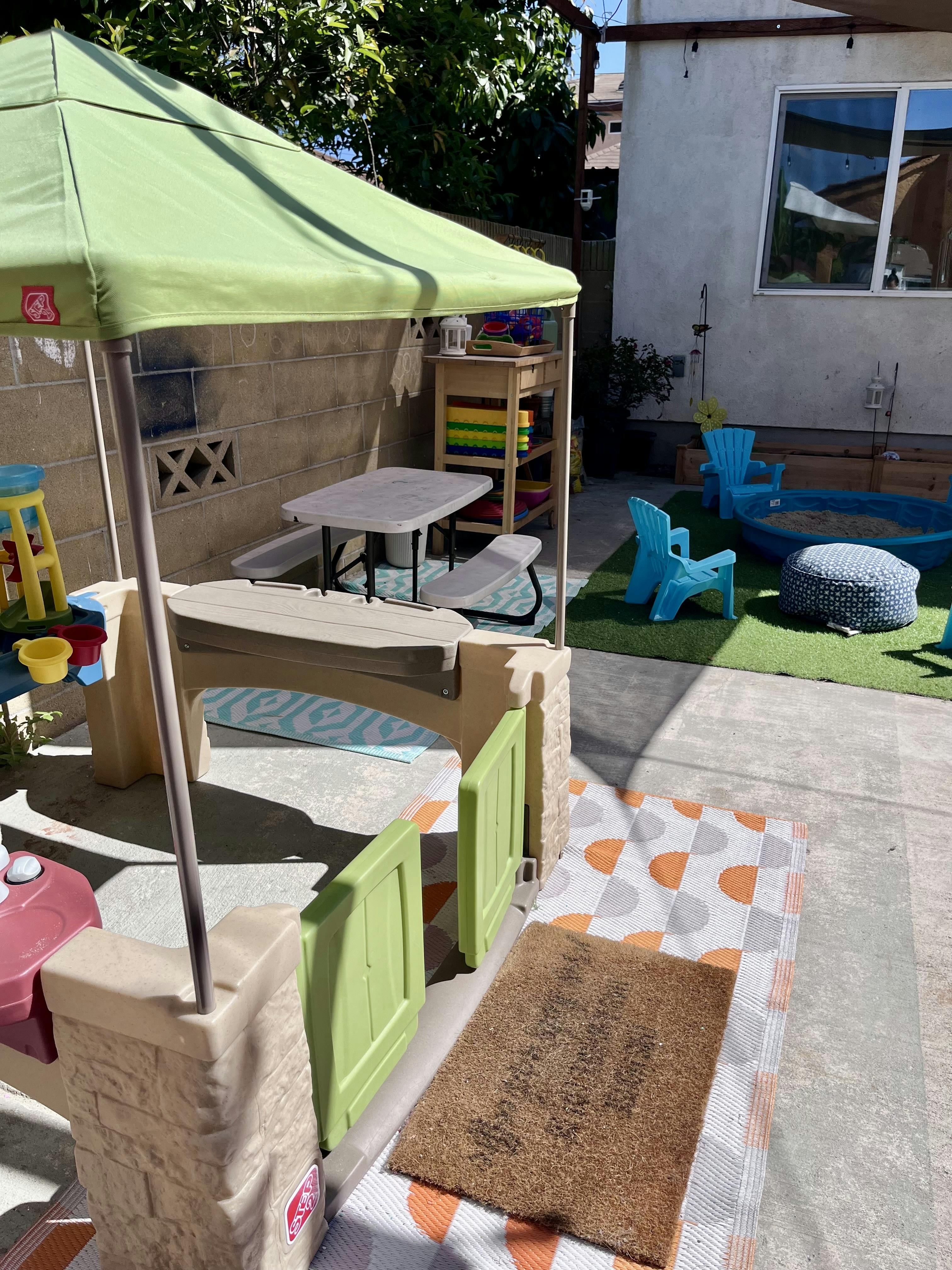 Outdoor play area with a playhouse, sandpit, and small chairs