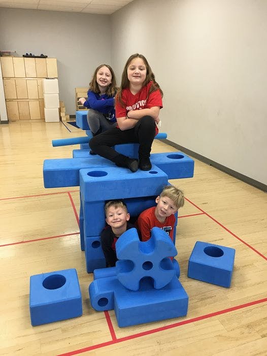 Two children sitting on large blue blocks, two children peeking from inside blocks
