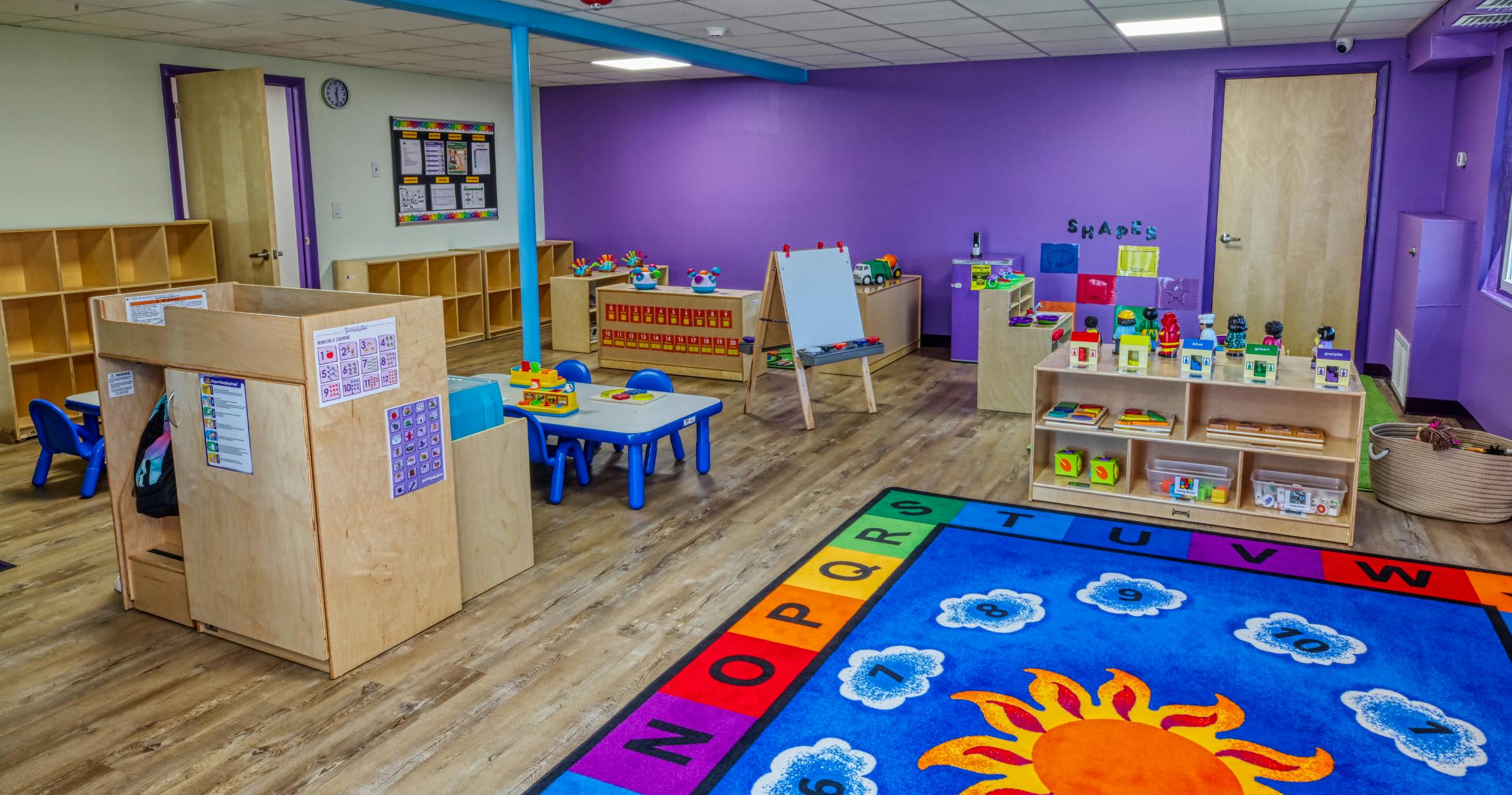 Colorful classroom with an alphabet rug, small tables and chairs, and shelving units