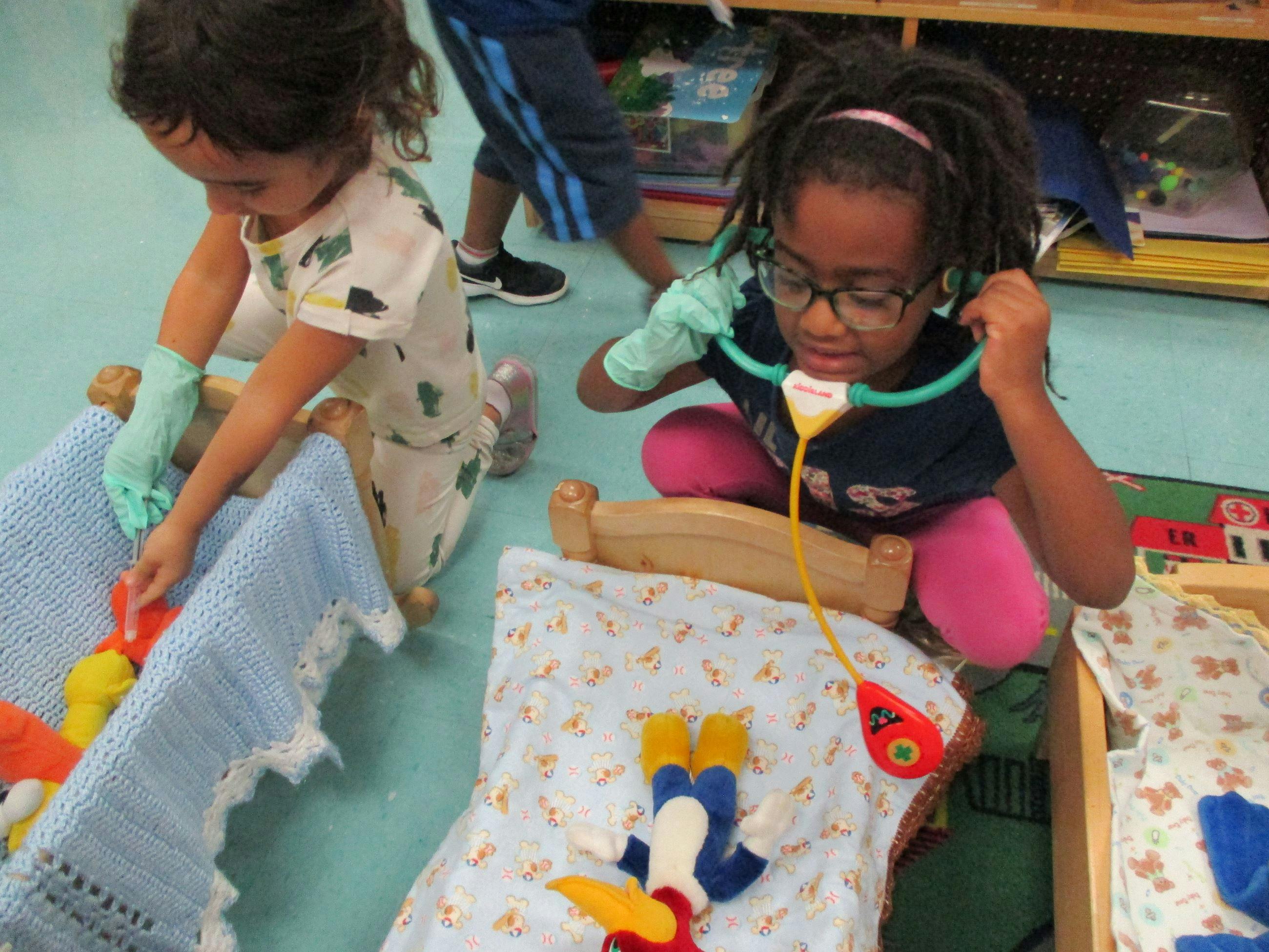 Two children playing with toy beds and a stethoscope