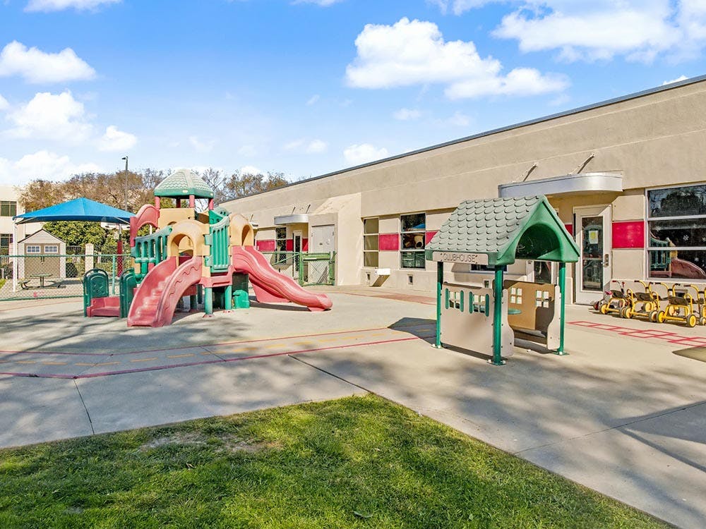 Empty playground with colorful slides, climbing structure, and playhouse next to a building