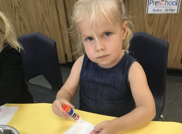 Child holding a glue stick at a table
