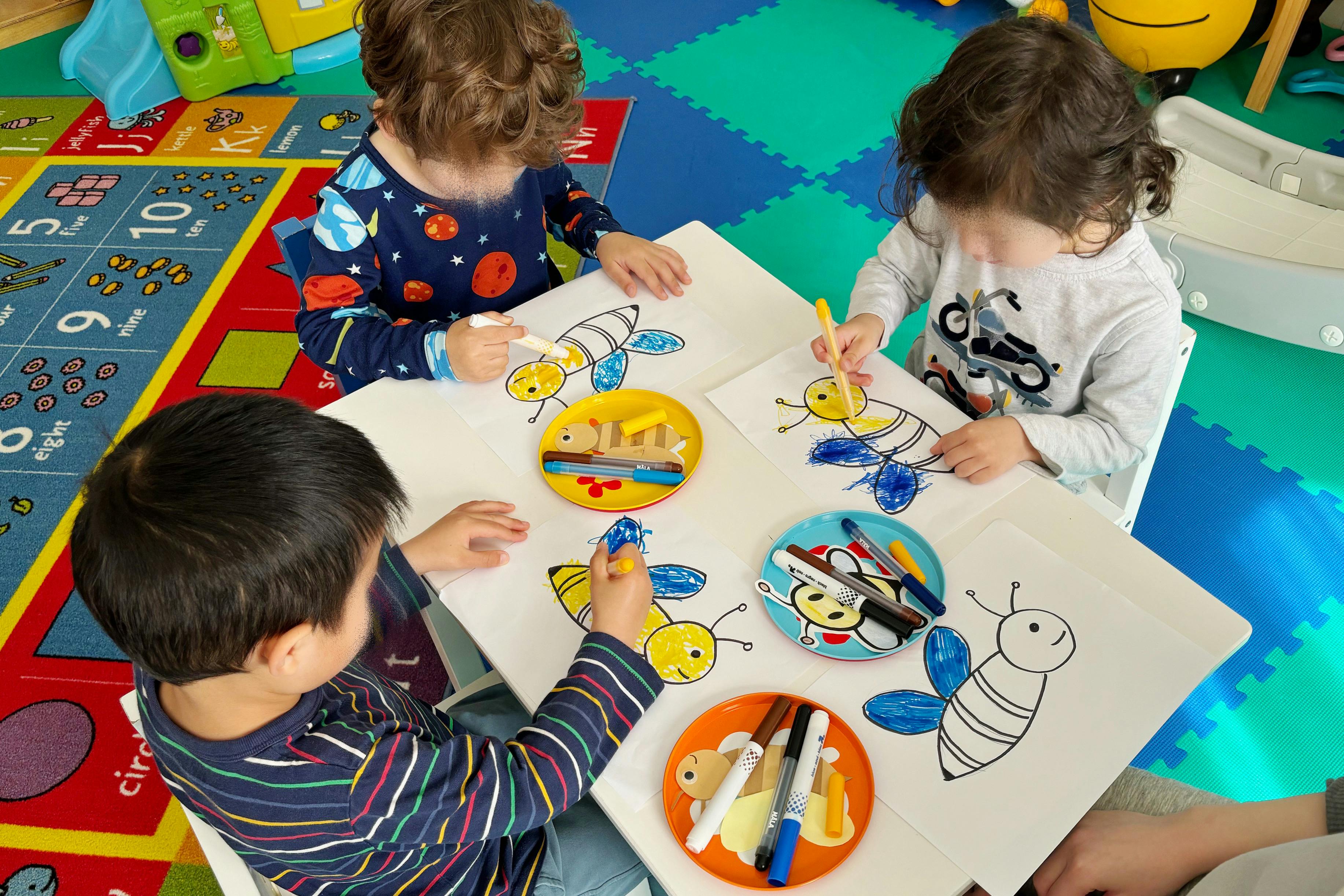 Three children drawing bee pictures at a table