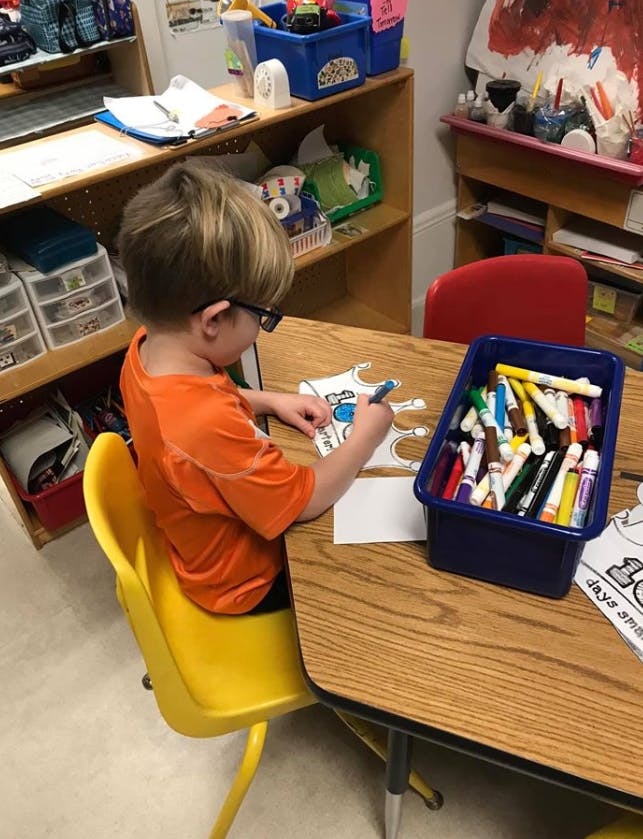 Child in glasses coloring at a table with markers