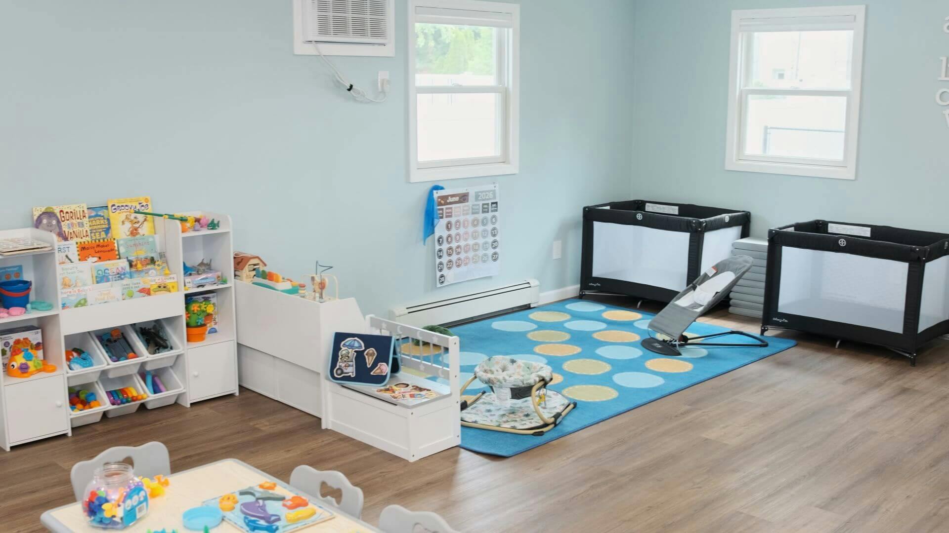Childcare room with play mats, books on a shelf, and portable cribs