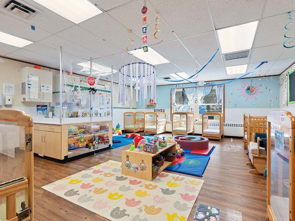 A brightly lit nursery room with multiple cribs and play areas