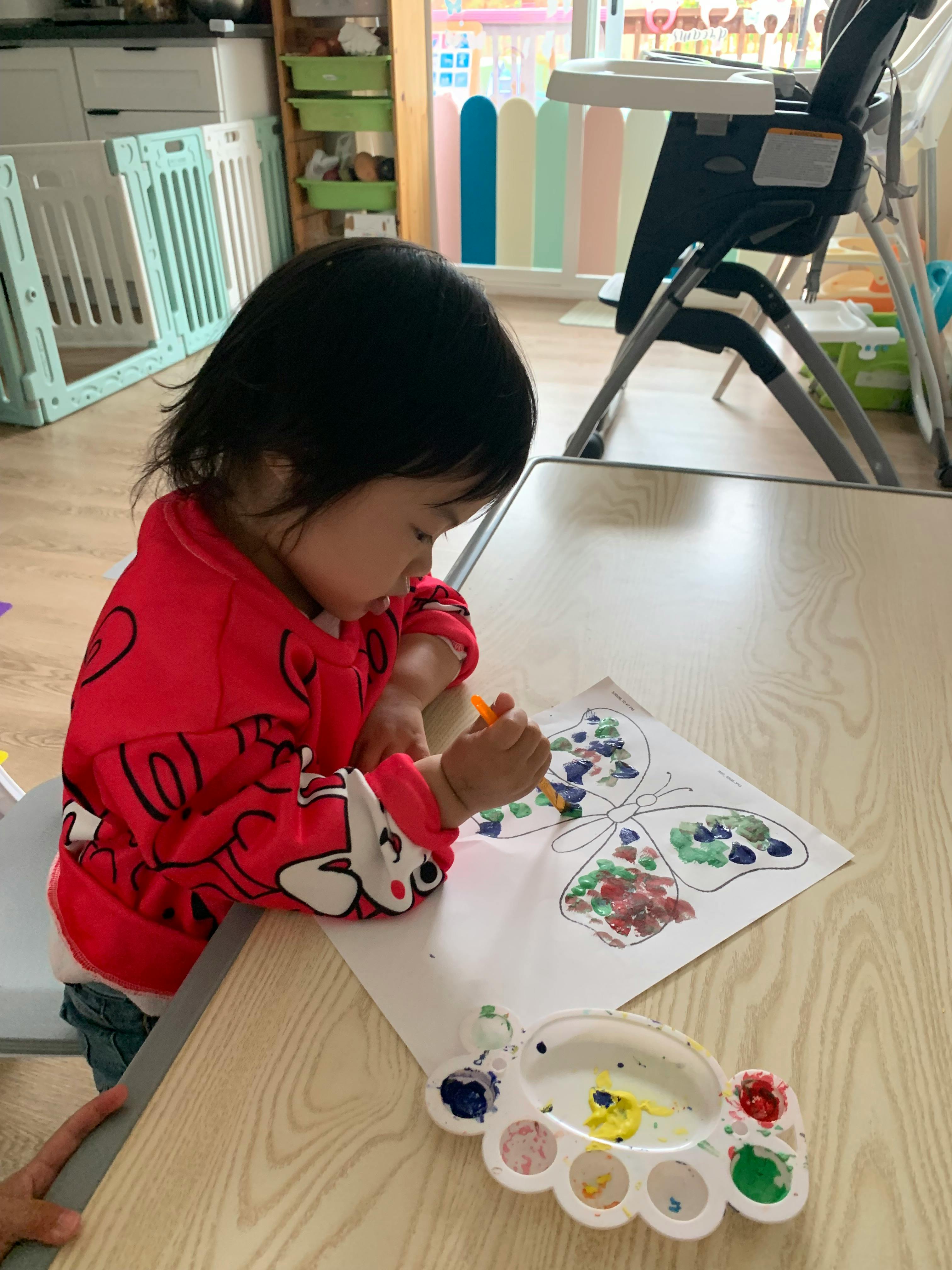 Child painting a butterfly drawing at a table