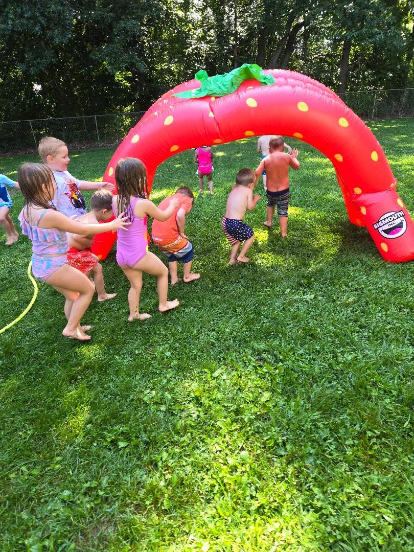 Children playing in a yard with a large inflatable strawberry arch