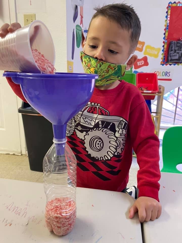 Child pouring small red objects from a cup into a funnel and bottle