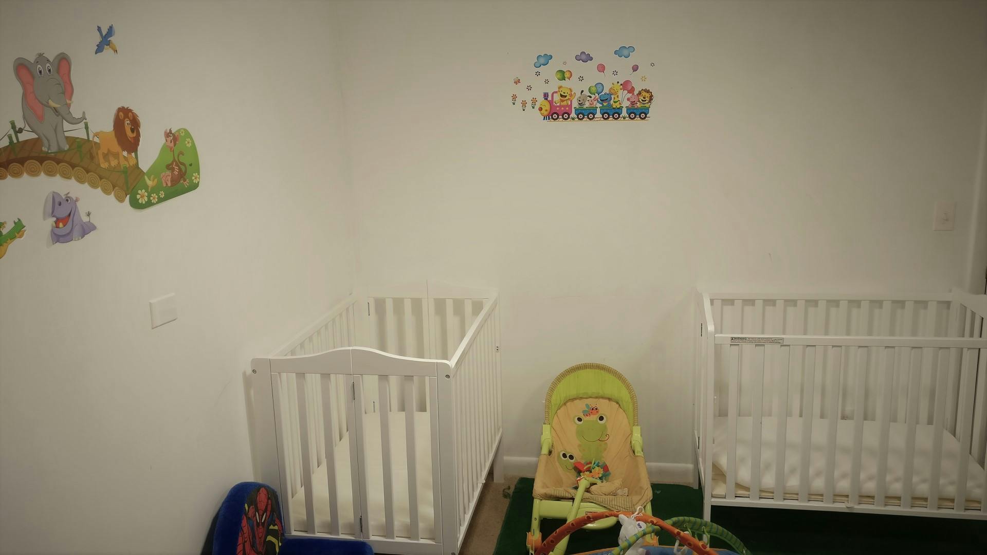 Two white cribs and a baby bouncer in a room with wall decals