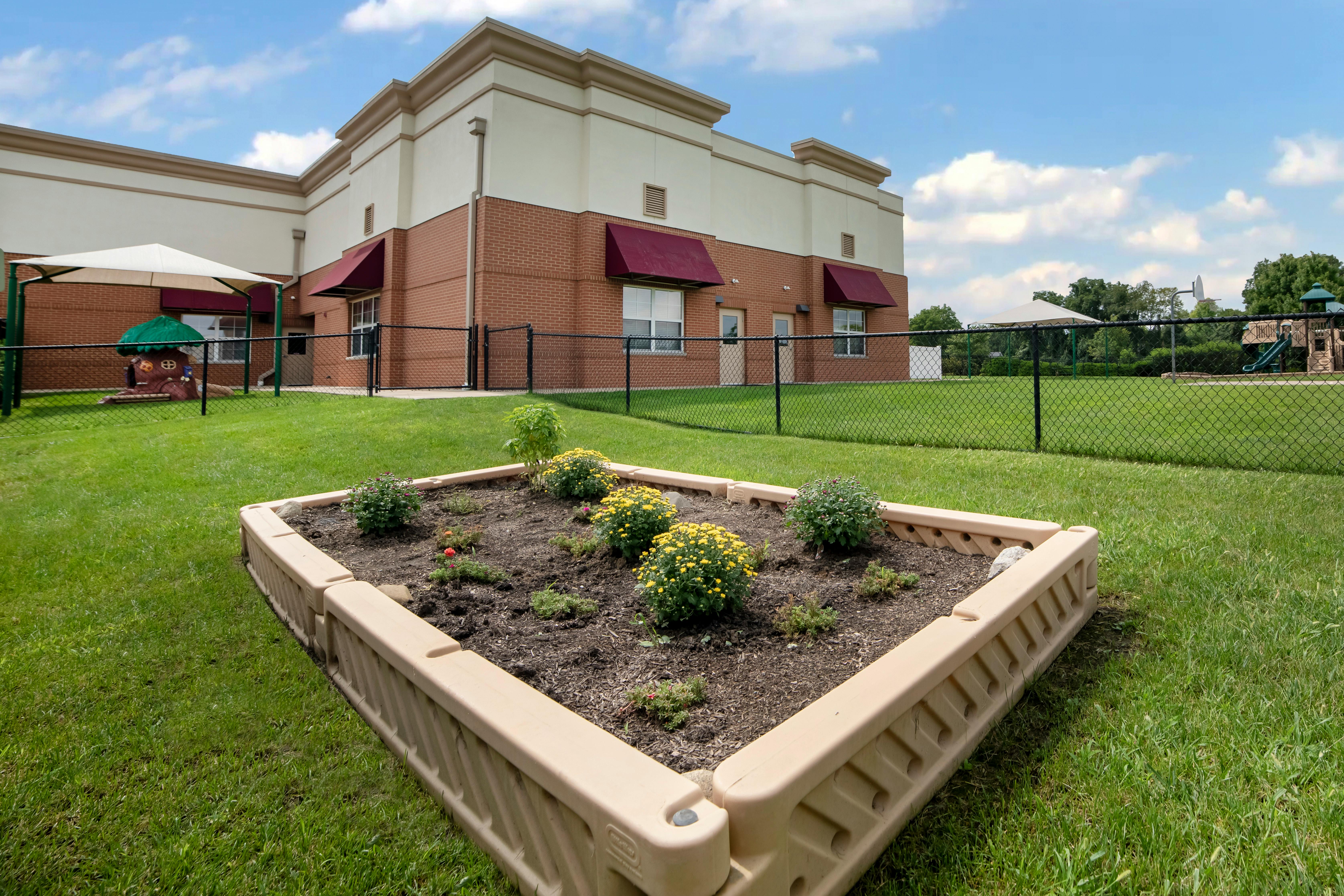 Raised garden bed with flowers and playground area next to a brick building