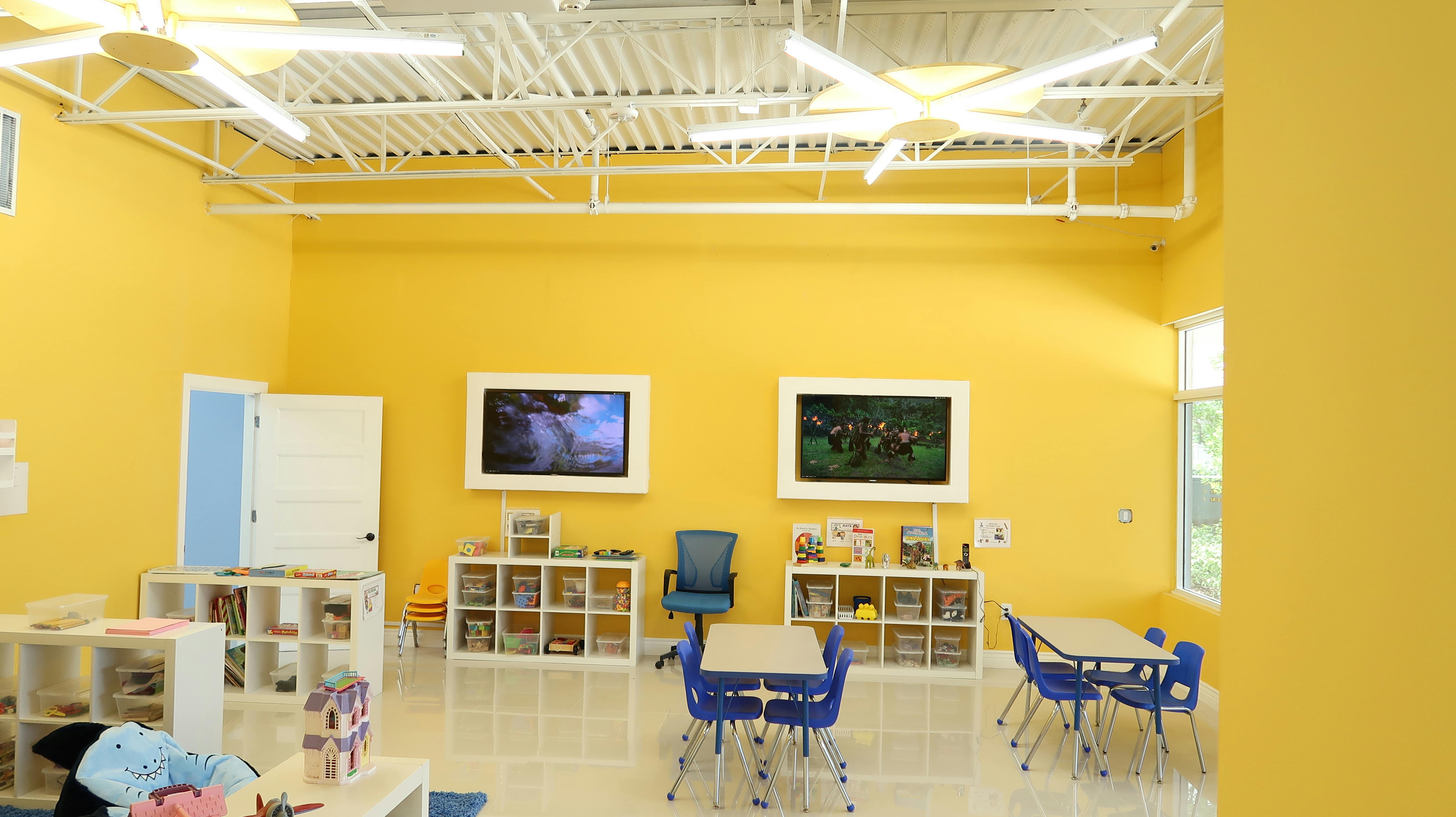 Classroom with yellow walls, tables, chairs, and shelves