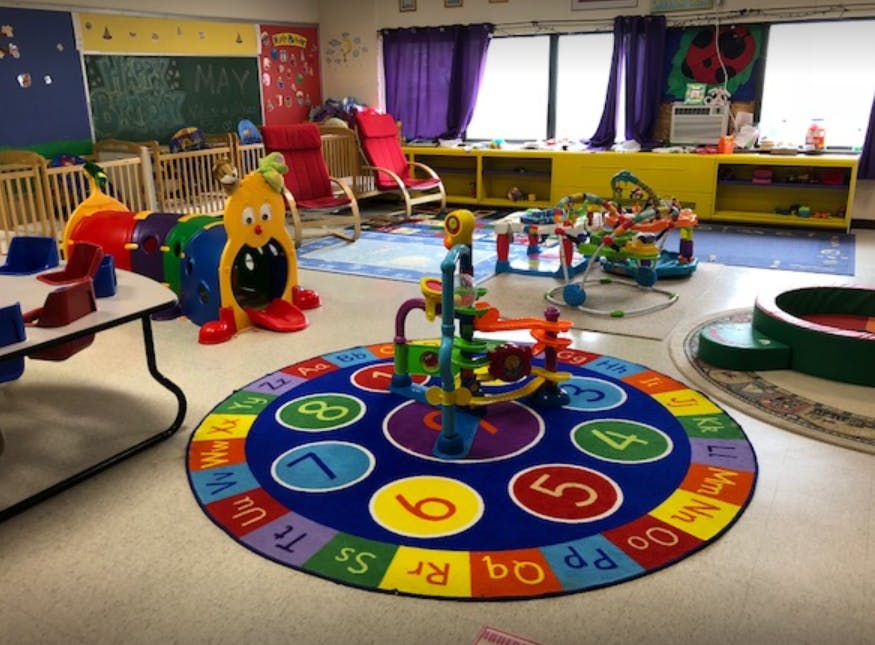 Playroom with a colorful number and alphabet rug, toys, and cribs