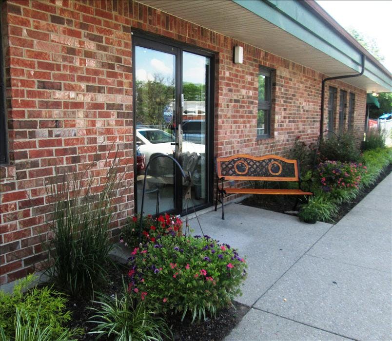 Brick building exterior with glass doors, a wooden bench, and landscaping