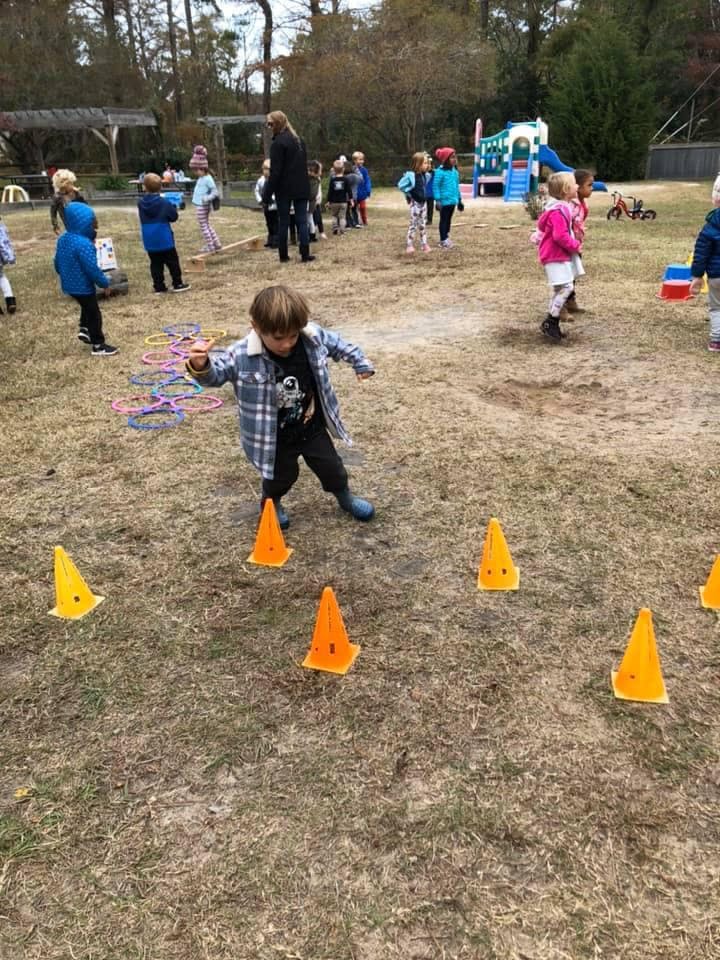 Child walking through orange cones on a grassy field with other children in background