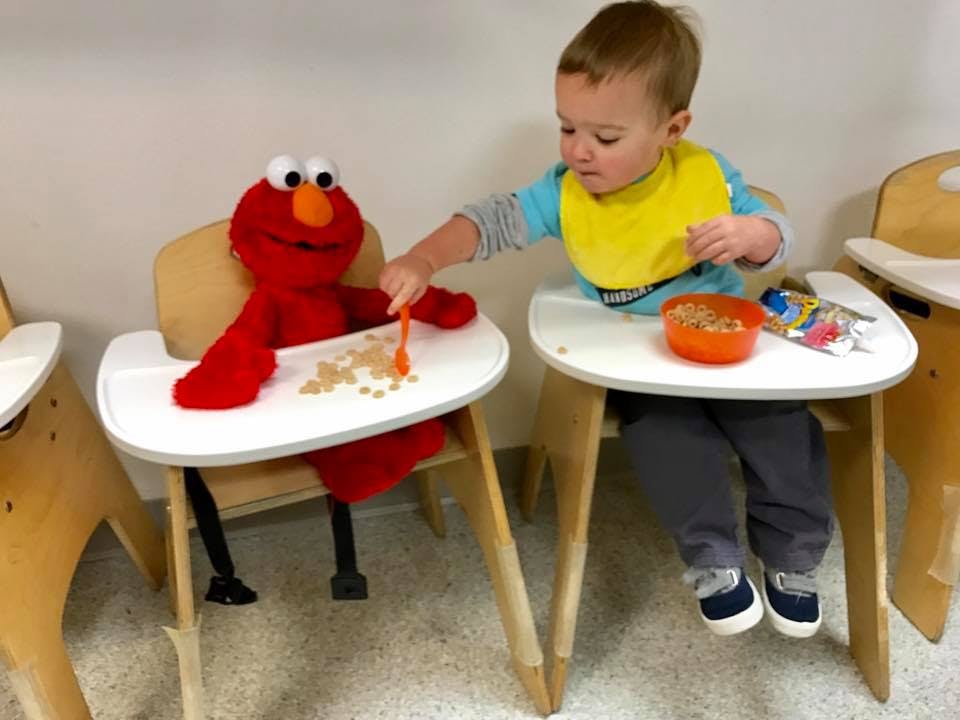 Child in high chair feeding a toy in a high chair