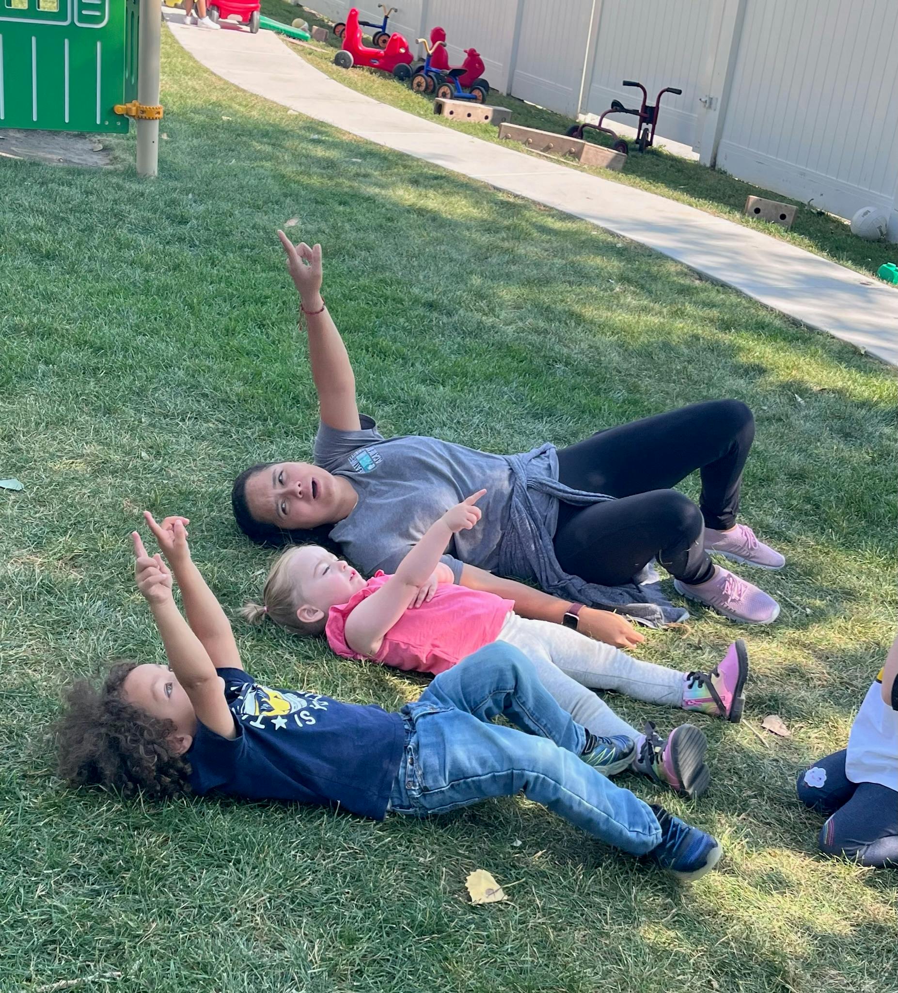 Adult and two children lying on grass pointing up