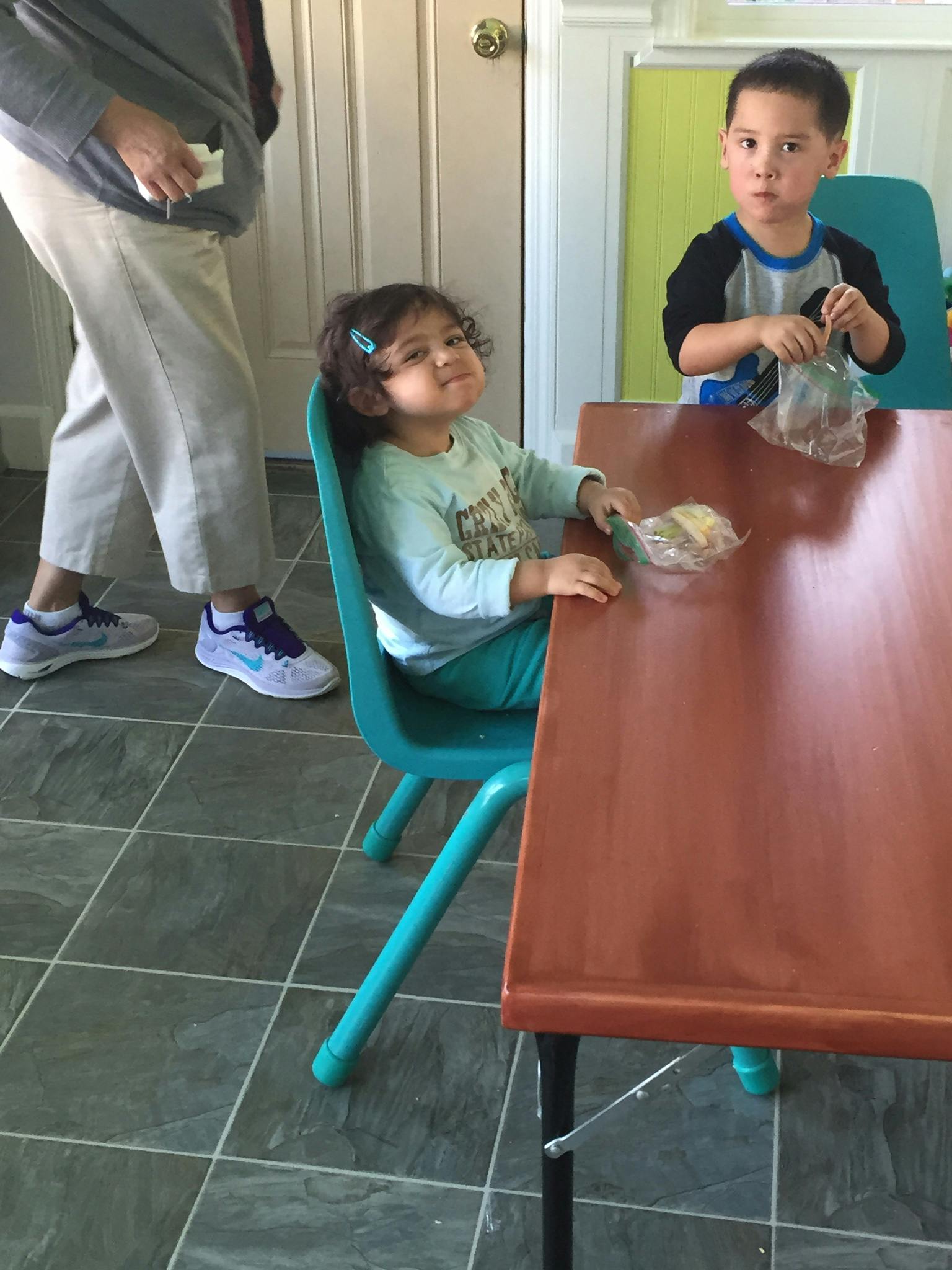 Two children at a table, one holding a bag, the other with a spoon