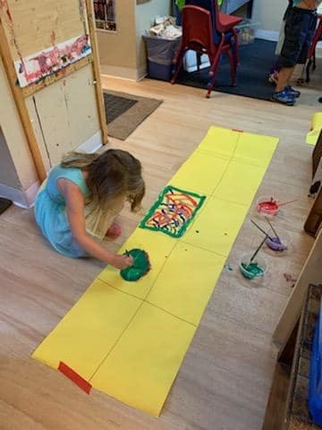 Child painting on a long yellow paper on the floor