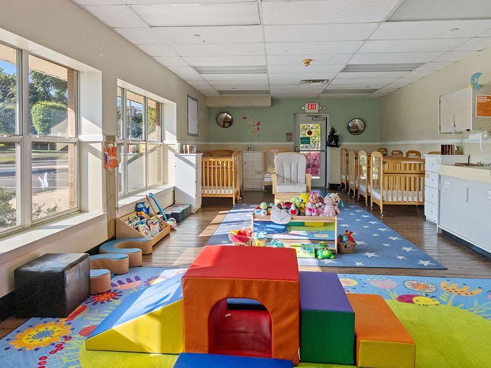 Playroom with soft play equipment, cribs, and large windows