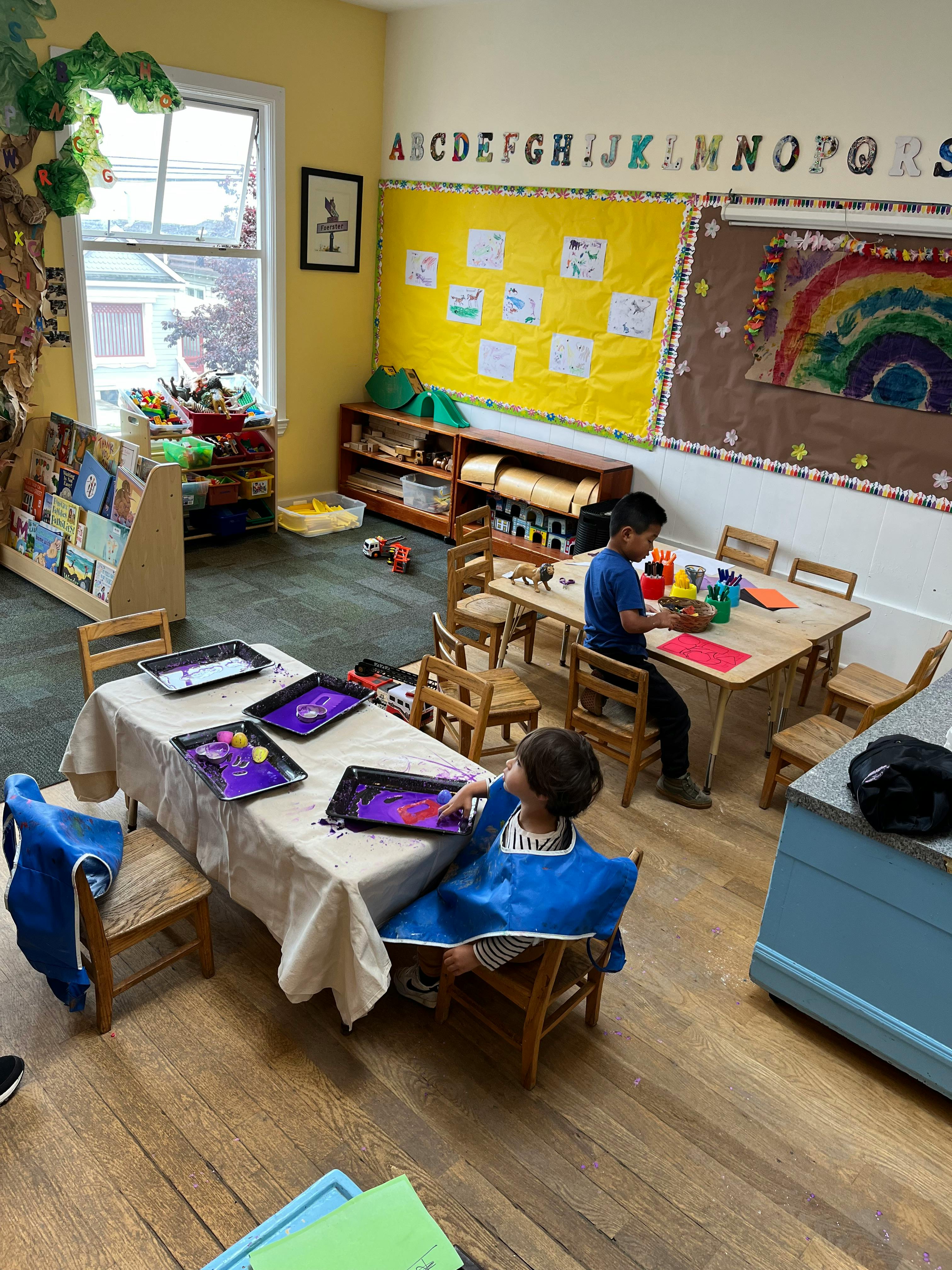 Two children painting at tables in a classroom
