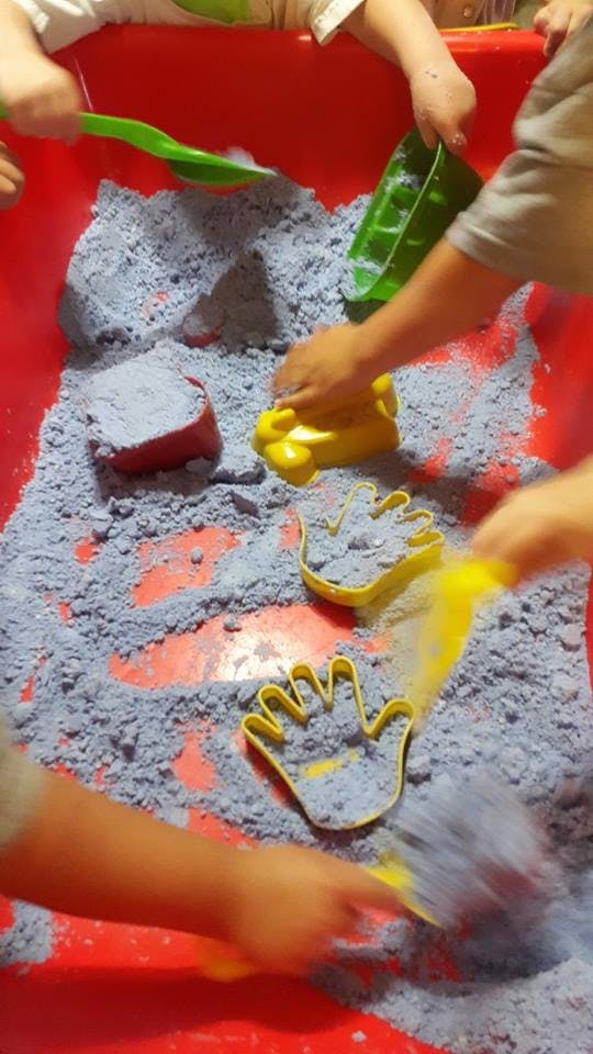 Children playing with kinetic sand and molds in a red bin