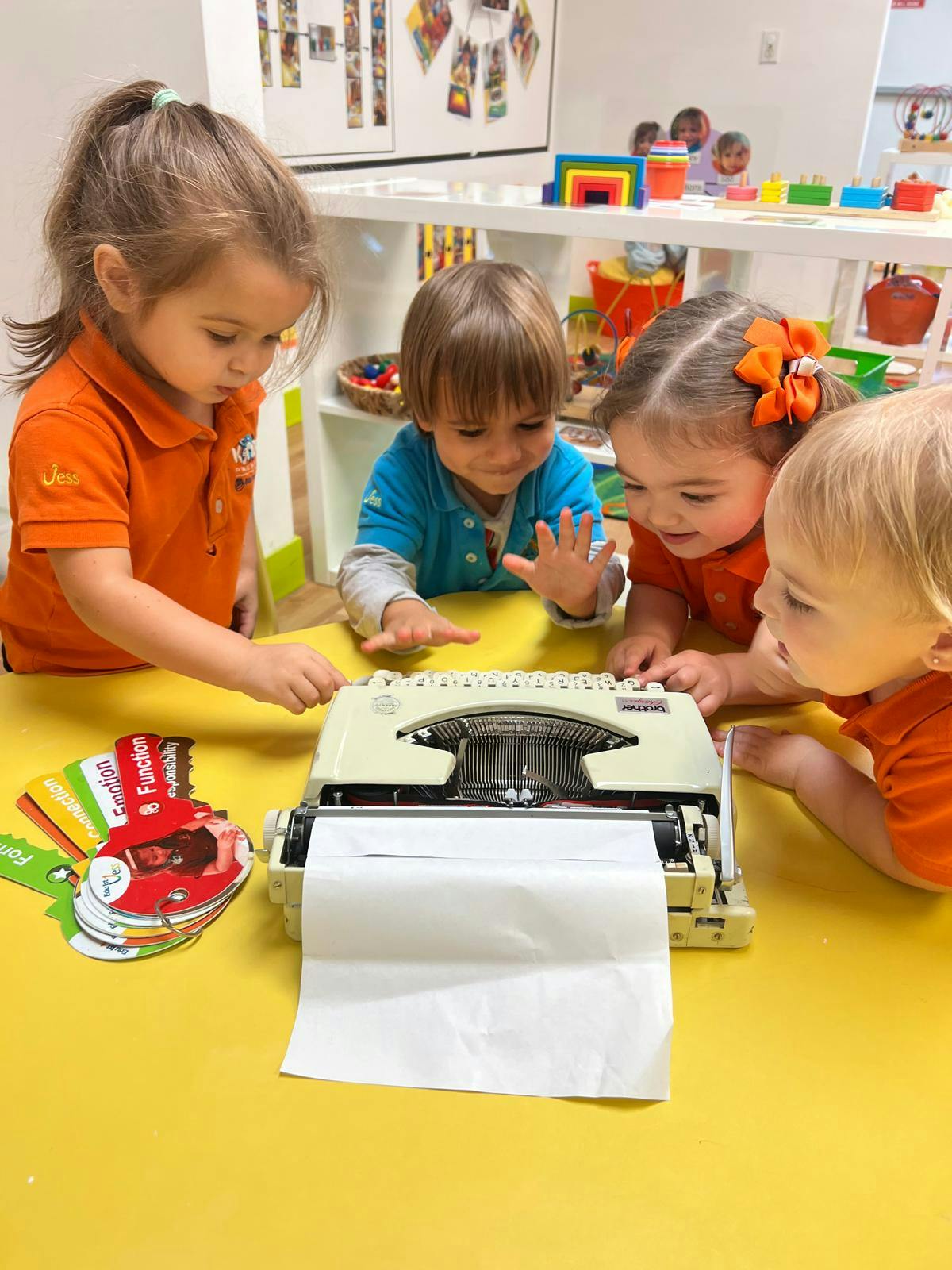 Children gathered around a typewriter on a yellow table
