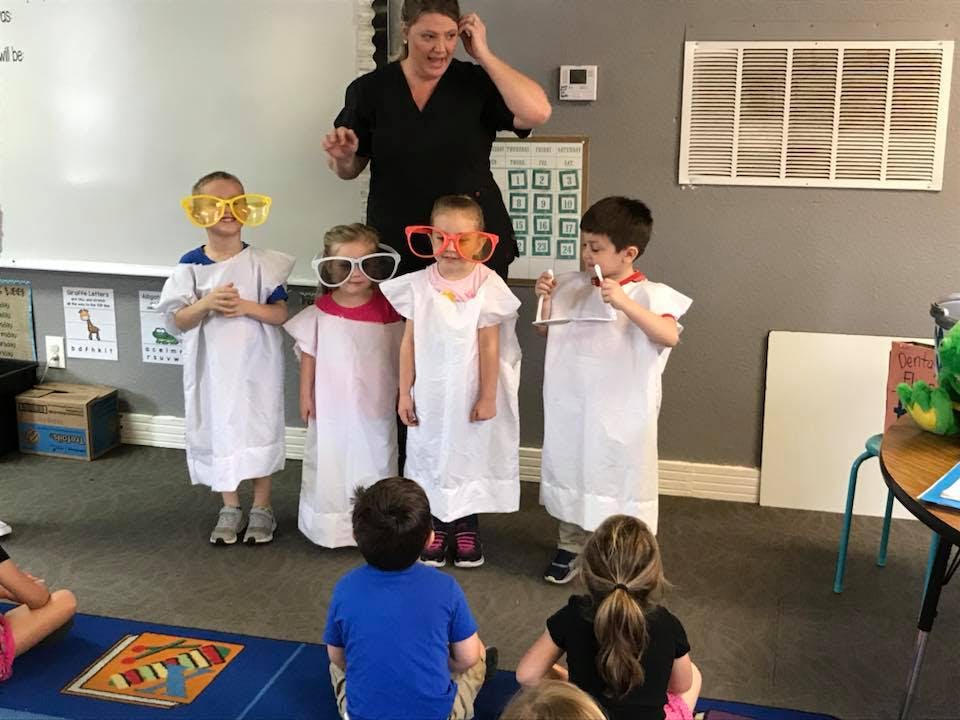 Adult and children in white smocks and novelty glasses in a classroom
