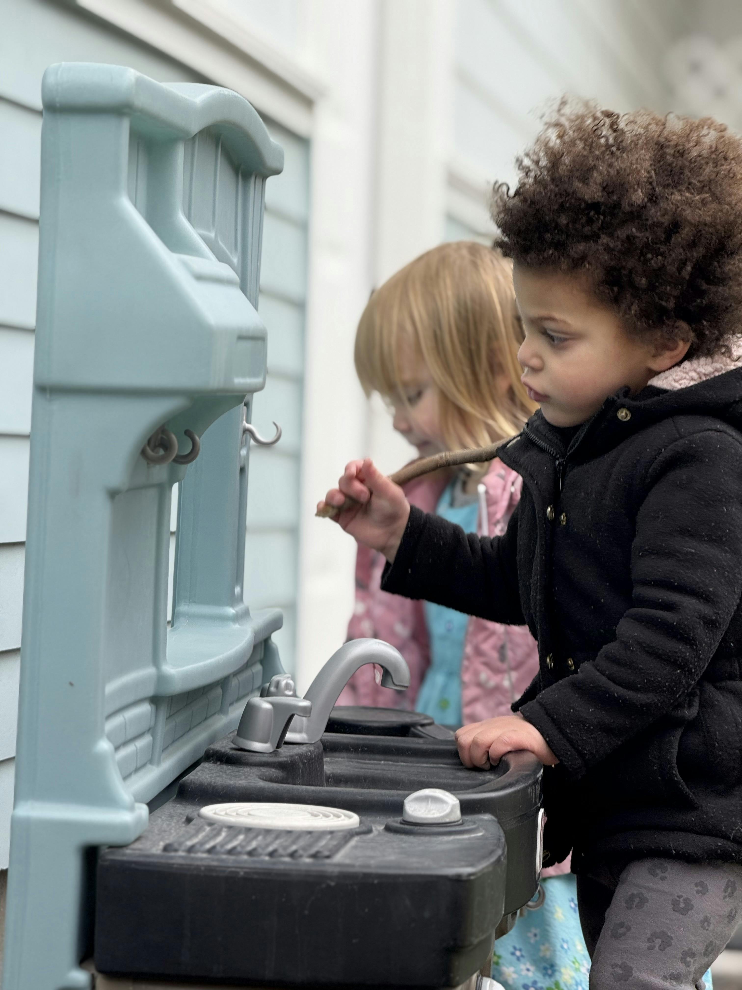 Two children playing with a toy kitchen set outdoors