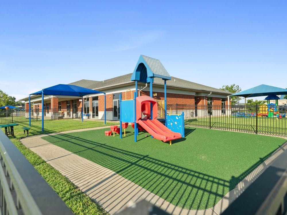 Playground with blue and red equipment on green turf in front of a brick building