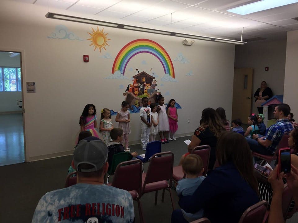 Children performing in front of an audience with a rainbow mural