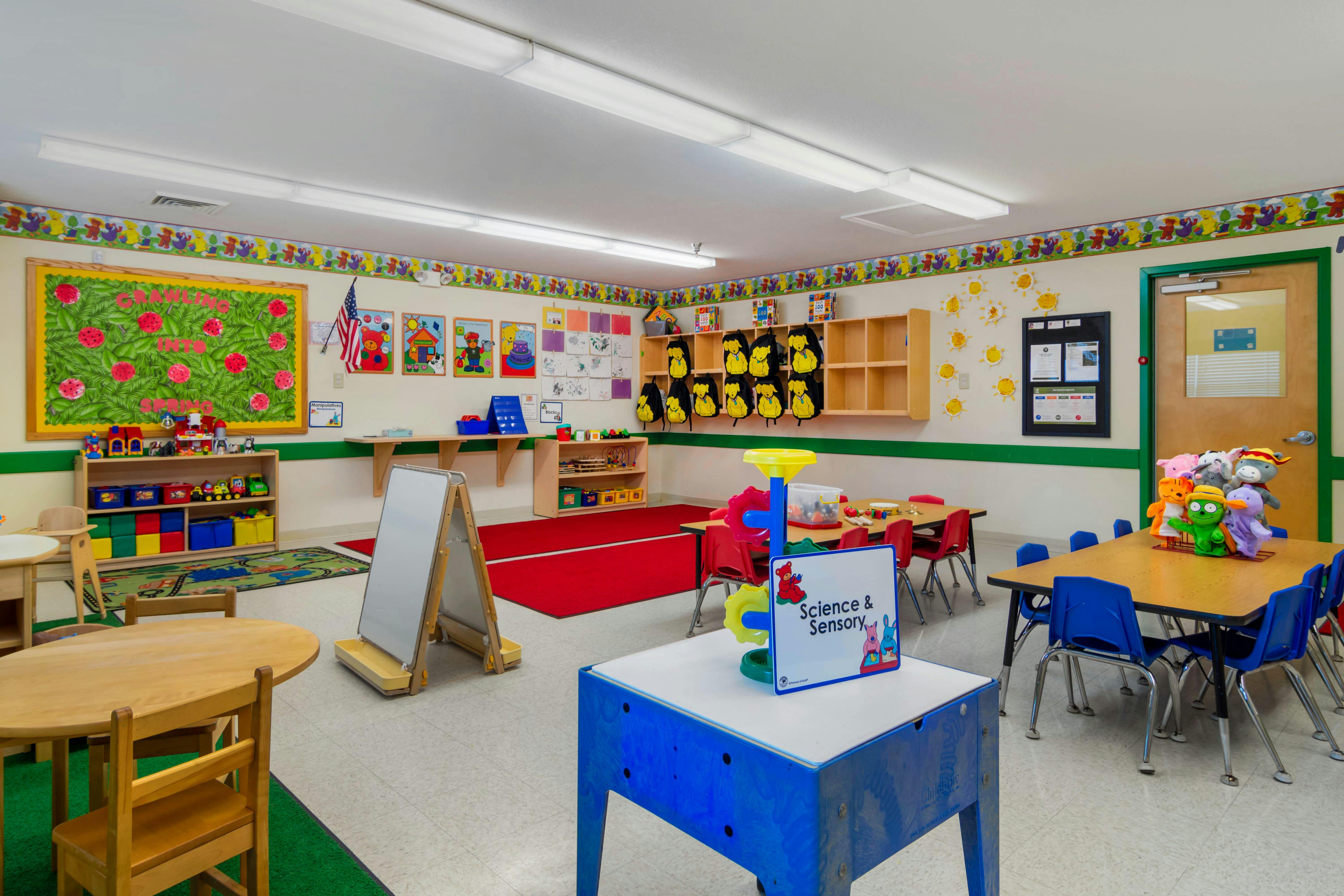 A classroom with small tables and chairs, shelves, and decorations on the walls
