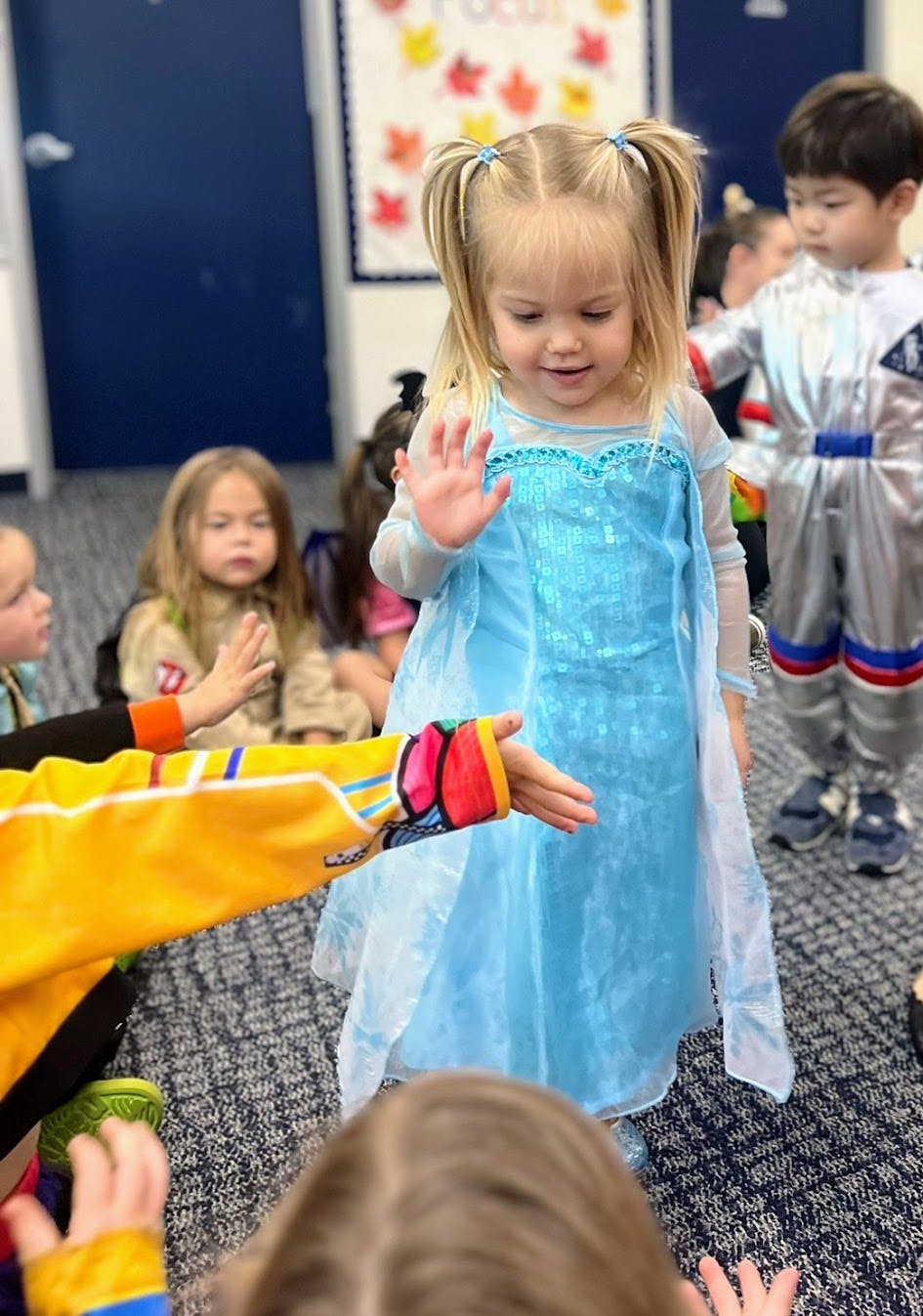 Child in blue dress high-fiving another child in a classroom