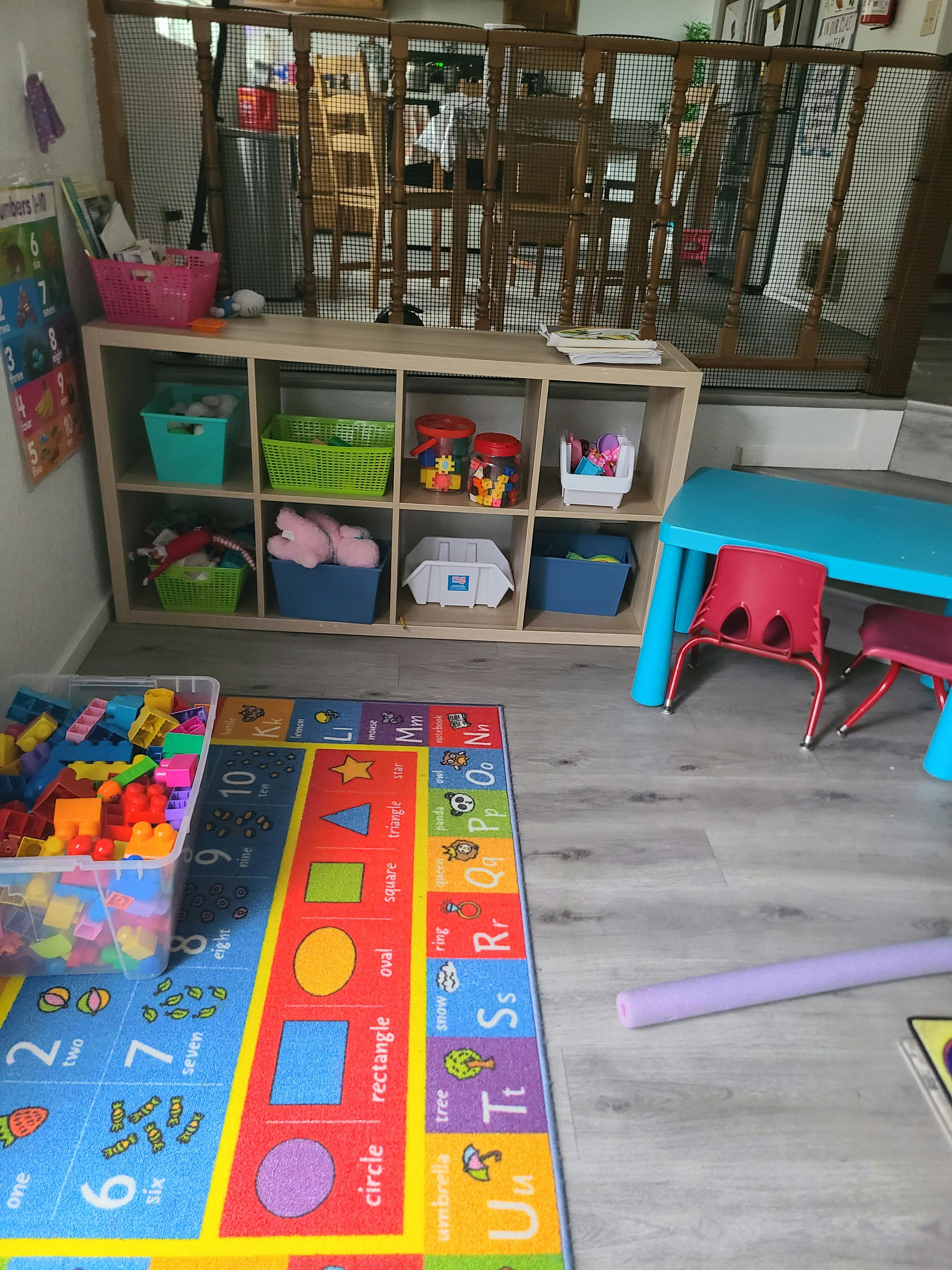 Children's play area with a colorful alphabet rug, toy shelves, and small table