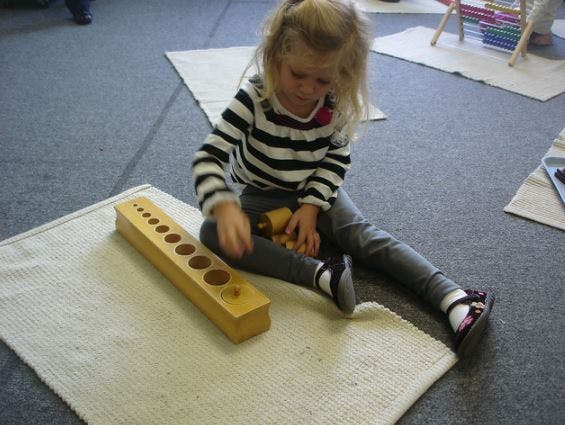 Child playing with a wooden cylinder block puzzle on a rug