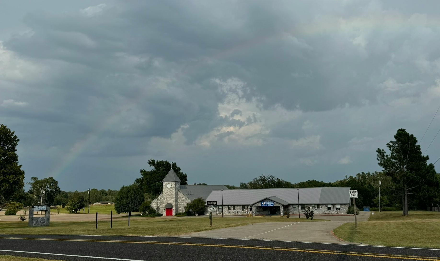 Church building with a steeple and a long, low addition under a cloudy sky