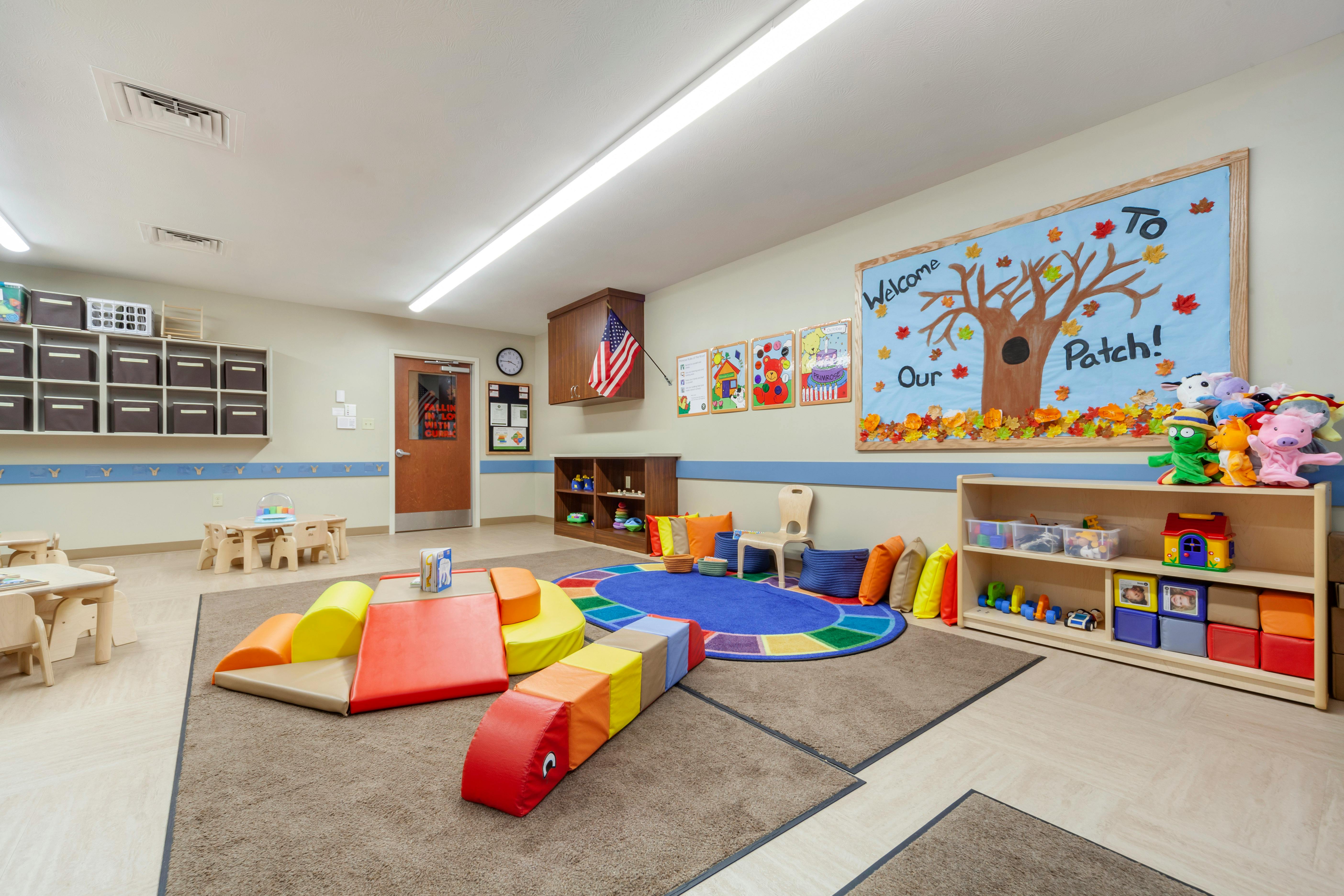 A colorful playroom with child-sized tables, shelves, and a fall-themed bulletin board