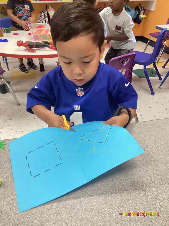 Child cutting shapes out of blue paper with scissors in a classroom