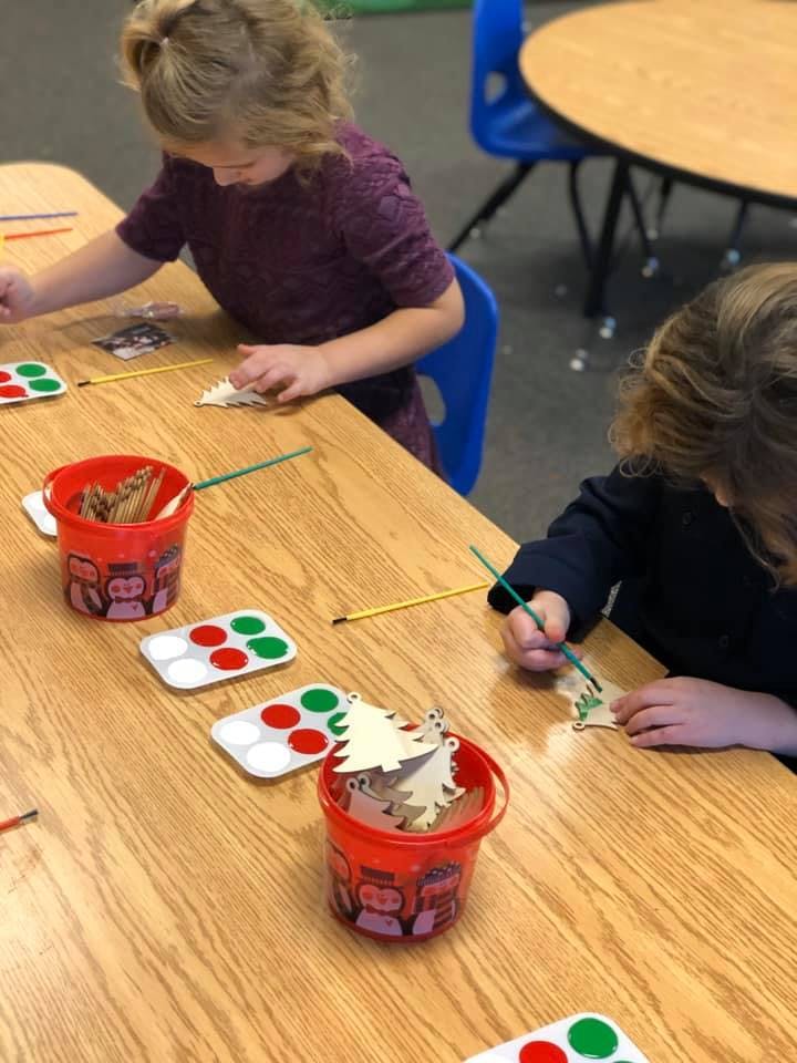 Two children painting wooden cutouts at a table