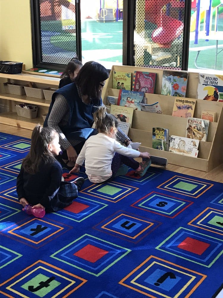 Adult and two children sitting on a rug looking at books in a classroom