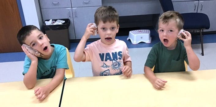 Three children sitting at a table with hands to their ears