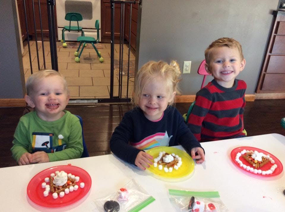 Three children sitting at a table with plates of food
